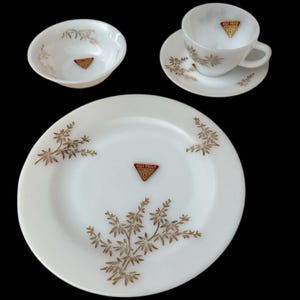 May include: A white vintage dish set with gold floral accents. The set includes a bowl, a teacup with saucer, and a dinner plate. Each piece has a gold "Heat Proof" emblem.