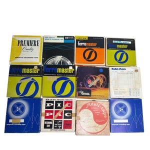 May include: A collection of vintage magnetic recording tape boxes in various colors, including yellow, orange, and blue. The boxes feature brand names like "FerroMaster" and "Premiere Quality," with graphic designs and text. The tapes are for audio recording.