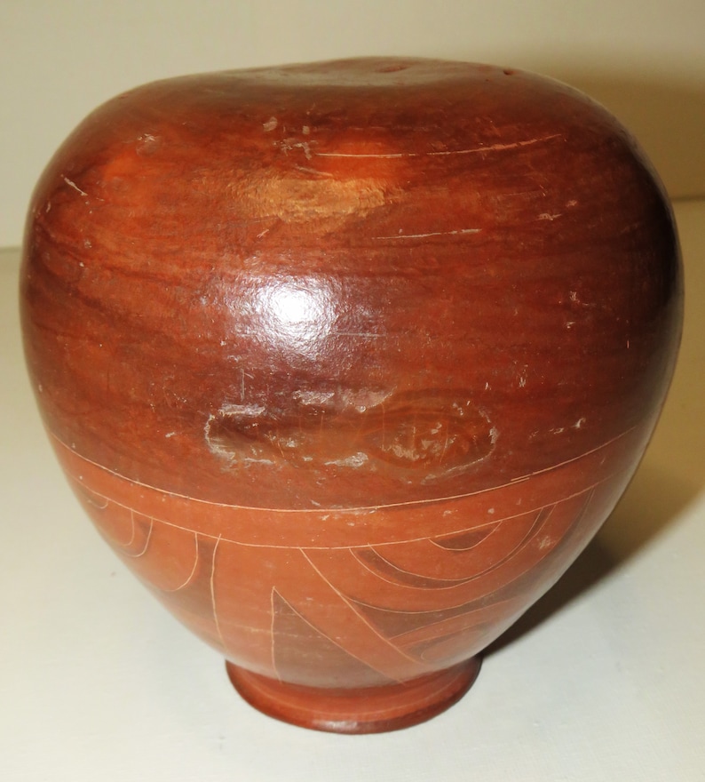 May include: A terracotta pottery vase with a geometric design in a lighter shade of terracotta. The vase is round with a slightly wider base and a narrow neck.