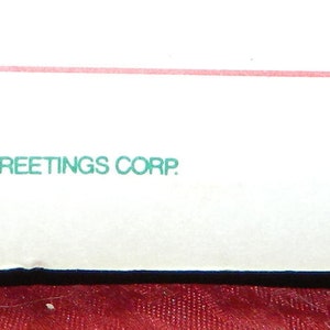 May include: White rectangular card with the text "&copy;MCMLXXXV AMERICAN GREETINGS CORP. MADE IN HONG KONG" and a red rose logo. The card has a torn corner with the text "SA-506B".