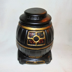 Puede incluir: Jarrón de cerámica negro con forma de estufa de leña con ribete dorado y una ventana con un diseño rojo y naranja.