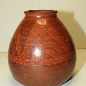May include: A brown ceramic vase with geometric designs in a lighter brown color. The vase has a rounded body and a slightly flared opening.