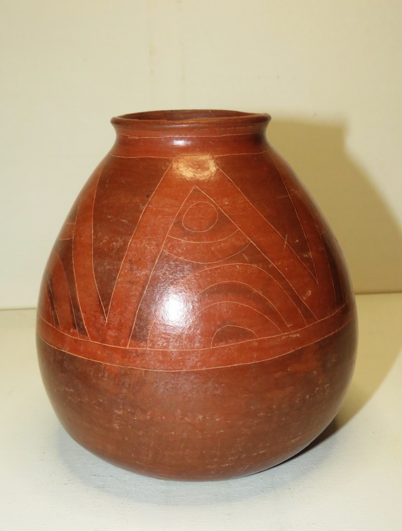 May include: A brown ceramic vase with geometric designs in a lighter brown color. The vase has a rounded body and a slightly flared opening.