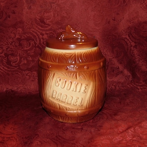 Pode incluir: Jarro de biscoitos de cerâmica marrom em forma de barril com textura de madeira e as palavras "COOKIE BARREL" na frente.