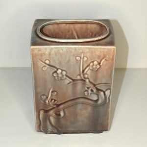 May include: A square ceramic vase with a brown and grey glaze. The vase features a raised design of a flowering branch.