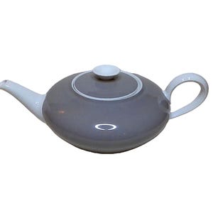 May include: A gray ceramic teapot with a white handle, spout, and lid. The teapot has a rounded body with a white ring around the lid. The lid has a small white knob. The teapot is designed for brewing tea.