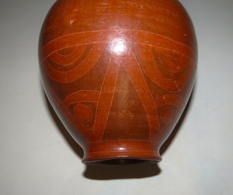 May include: A brown ceramic vase with a geometric design. The vase has a rounded body and a narrow neck.
