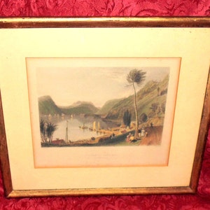May include: A framed print depicting a landscape scene with a river, mountains, and trees. The print is in a gold frame and has a white mount.