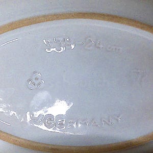 Puede incluir: Un plato ovalado de cer&aacute;mica blanca con un borde marr&oacute;n claro. La base del plato tiene texto en relieve que dice "W. Germany" y otras marcas. El plato es probablemente vintage.