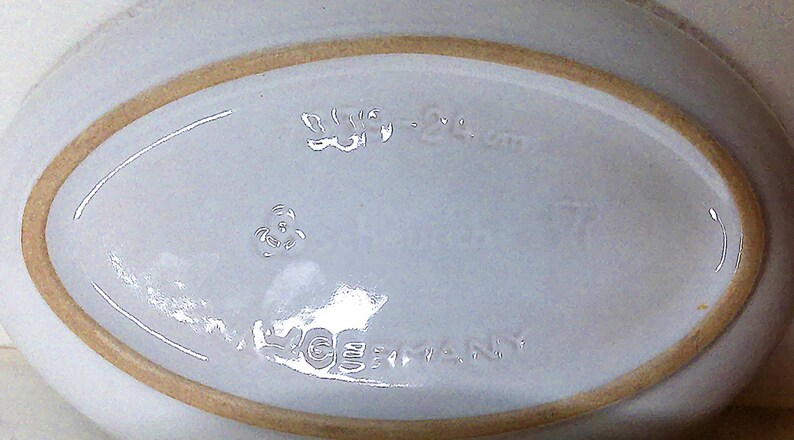 Puede incluir: Un plato ovalado de cer&aacute;mica blanca con un borde marr&oacute;n claro. La base del plato tiene texto en relieve que dice "W. Germany" y otras marcas. El plato es probablemente vintage.
