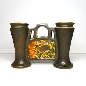 Könnte beinhalten: Eine braune Keramik-Doppelvase mit einem Blumendesign in Gelb-, Grün- und Brauntönen. Die Vase hat zwei Öffnungen für Blumen und einen dekorativen Ausschnitt in der Mitte.