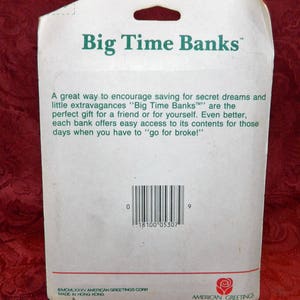 May include: White cardboard packaging for "Big Time Banks" with green text. The text includes the brand name and a description of the product. A barcode and the American Greetings logo are also visible.