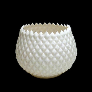 May include: A white, textured ceramic vase with a diamond pattern and a jagged rim. The vase has a rounded shape and is set against a black background. The vase is likely used for decorative purposes.