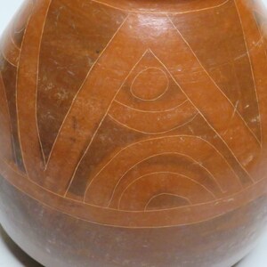 May include: A brown ceramic pot with a geometric design. The design features a series of concentric circles and triangles, all carved into the surface of the pot.
