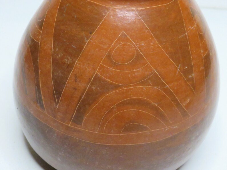 May include: A brown ceramic pot with a geometric design. The design features a series of concentric circles and triangles, all carved into the surface of the pot.