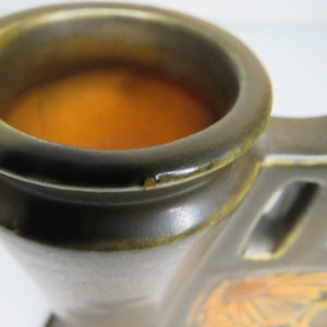 Może przedstawiać: Zbliżenie na brązowy ceramiczny świecznik z jednym okrągłym otworem na g&oacute;rze. Otw&oacute;r jest wypełniony jasno pomarańczowym woskiem.