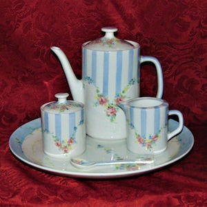 Könnte beinhalten: Ein weißes Teeservice mit blauen Streifen und floralen Akzenten. Das Set beinhaltet eine Teekanne, eine Milchkännchen, eine Zuckerdose und einen kleinen Löffel. Das Set befindet sich auf einem weißen Tablett mit blauem Rand.