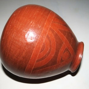 May include: A red clay pot with a geometric design incised into the surface. The design is made up of lines and circles.
