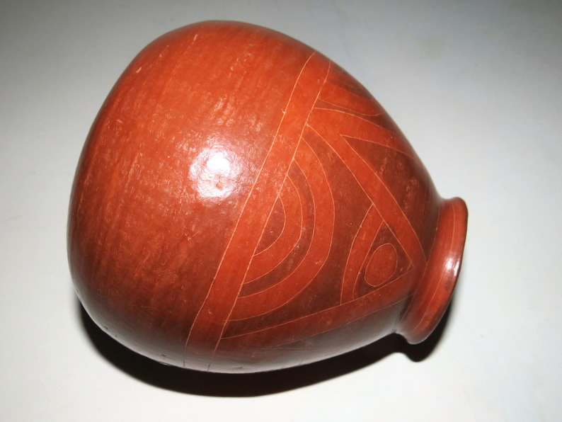 May include: A red clay pot with a geometric design incised into the surface. The design is made up of lines and circles.