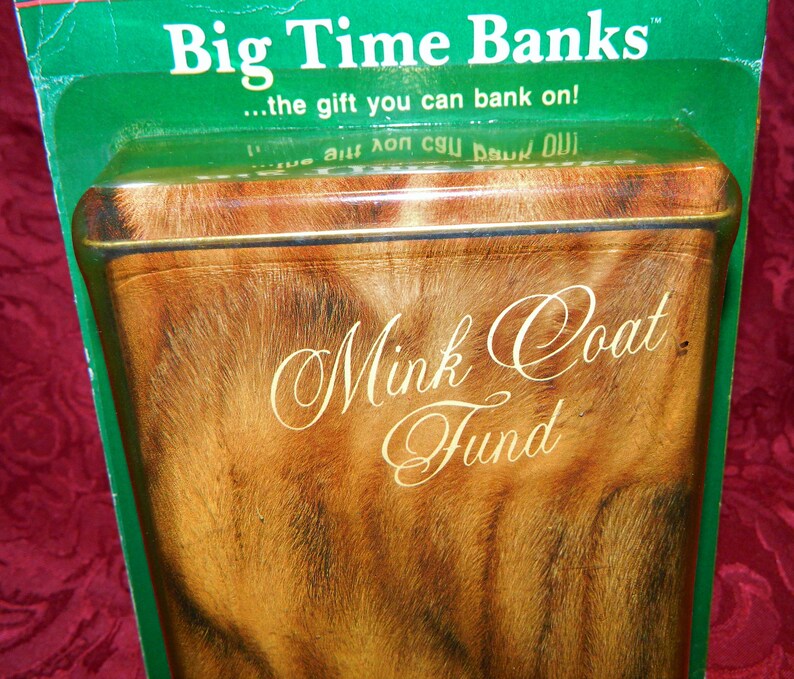 May include: A rectangular bank with a mink coat design. The bank has the words "Mink Coat Fund" in elegant script. The top of the bank is visible, with the words "Big Time Banks" and "...the gift you can bank on!" printed on the green packaging.