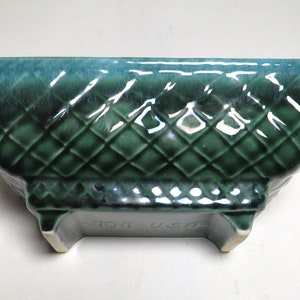 May include: A green glazed ceramic planter with a diamond pattern and a raised base. The planter has the text "404 - USA" on the bottom.