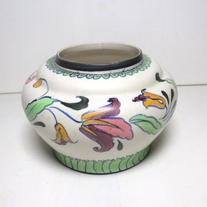 May include: A white ceramic planter with a green, yellow, and pink floral design. The planter has a rounded shape and a slightly flared rim.