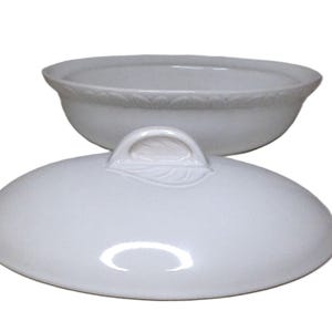 Puede incluir: Una fuente de cer&aacute;mica blanca con tapa. La fuente tiene forma redondeada con un borde decorativo. La tapa presenta un asa con dise&ntilde;o de hoja. Tanto la fuente como la tapa son brillantes y parecen estar hechas de porcelana.