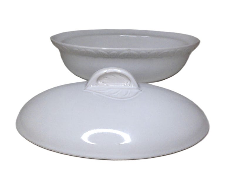 Puede incluir: Una fuente de cer&aacute;mica blanca con tapa. La fuente tiene forma redondeada con un borde decorativo. La tapa presenta un asa con dise&ntilde;o de hoja. Tanto la fuente como la tapa son brillantes y parecen estar hechas de porcelana.