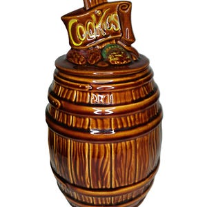Könnte beinhalten: Braune Keramik-Keksdose in Fassform mit vertikaler Holzmaserung. Der Deckel trägt die gelbe Aufschrift "Cookies". Ein Vintage-Küchenartikel.