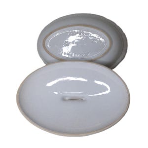 Puede incluir: Cazuela ovalada de cer&aacute;mica blanca con tapa. La tapa tiene un peque&ntilde;o asa. La parte inferior del plato tiene el texto "W. Germany". El plato es de color gris claro.