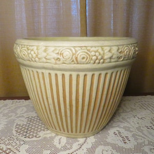 May include: A large, cream-colored ceramic planter with a ribbed design and a decorative floral border.