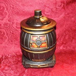 Puede incluir: Jarra de galletas de cerámica negra con forma de estufa de leña con detalles dorados y una puerta con estampado rojo y naranja.