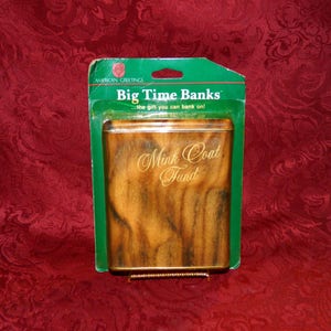 May include: A rectangular money bank with a faux mink coat design. The bank is in a green and clear plastic package. The text "Big Time Banks" and "Mink Coat Fund" are visible on the bank.