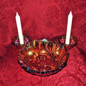 Peut inclure: Un ensemble de trois bougeoirs en verre iridescent avec un bol au centre. Les bougeoirs sont de couleur ambre foncé avec un reflet iridescent violet. Le bol est également de couleur ambre foncé avec un reflet iridescent violet. Les bougeoirs sont conçus pour contenir des bougies de taille standard.