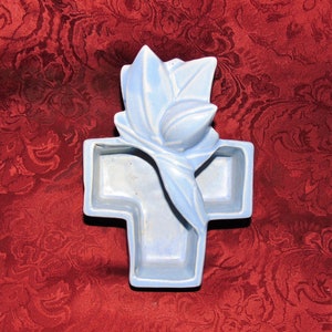 May include: A light blue ceramic cross shaped dish with a stylized flower design. The dish has three compartments.