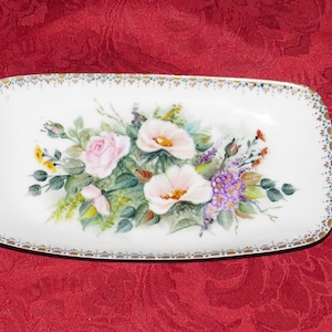 May include: A white rectangular ceramic dish with a gold trim and a hand-painted floral design featuring pink, white, and purple flowers.
