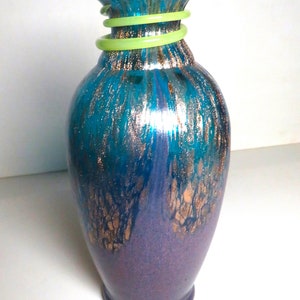 May include: A teal and purple glass vase with gold flecks and a green glass band around the neck.
