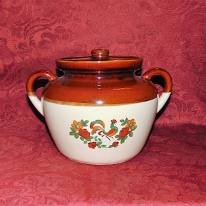 Puede incluir: Una olla de cerámica marrón y blanca con un gallo y un diseño floral. La olla tiene una tapa y dos asas.