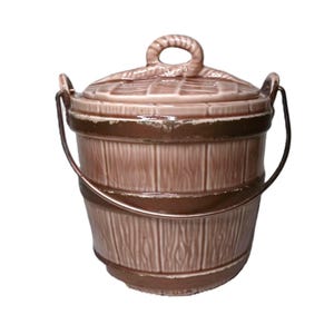 Könnte beinhalten: Keramik-Eimer mit Deckel, in Braun- und Beigetönen. Der Eimer hat eine Holzmaserung, einen Metallgriff und einen Seilgriff am Deckel. Das Design erinnert an einen Vintage- oder rustikalen Stil, ideal für die Küchenaufbewahrung.