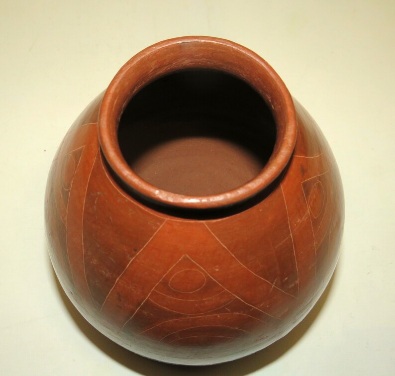 May include: A terracotta pot with a geometric design. The pot is brown and has a wide mouth.