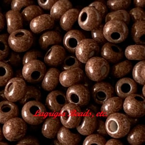 May include: A close-up image of a pile of brown seed beads. The beads are small and round, with a slightly textured surface. The beads are perfect for jewelry making or other craft projects.