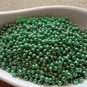 Könnte beinhalten: Nahaufnahme einer großen Menge kleiner, runder, grüner Glasperlen. Die Perlen haben eine glänzende, metallische Oberfläche.