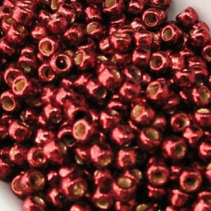May include: A close-up image of a white spoon filled with small, shiny, red beads. The beads have a metallic finish and are arranged in a random pattern.
