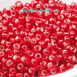 May include: A close-up image of a pile of small, red, glass beads. The beads are round and have a shiny, metallic finish.