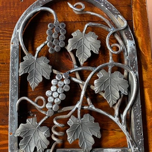 May include: A metal grapevine design with leaves and grapes. The design is made of metal and has a rustic look.