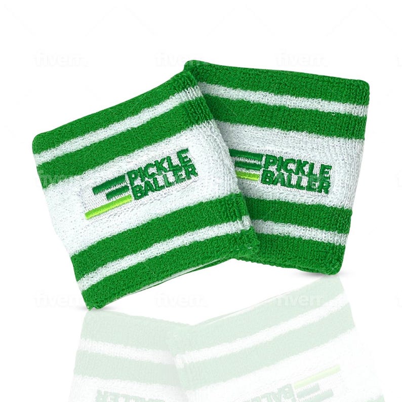 May include: Two white wristbands with green horizontal stripes. The text "PICKLE BALLER" is embroidered in green on each wristband. The wristbands are made of a soft, absorbent material, perfect for pickleball players.