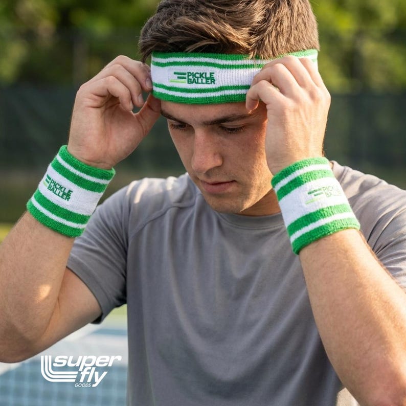 May include: White and green striped headband and wristbands. The headband and wristbands have the text "PICKLE BALLER" printed on them. The wristbands and headband are made of a soft, absorbent material.