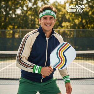 May include: A person wearing a retro-style tracksuit and holding a pickleball paddle. The paddle is white with a colorful wave design. The tracksuit is navy blue and cream with brown and red stripes. The image includes the text "SUPER FLY GOODS".