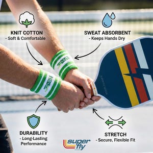 May include: White and green striped wristbands with the text "PICKLE BALLS" are worn by a person holding a pickleball paddle. The paddle is blue with yellow, red, and white stripes. The wristbands are knit cotton and sweat absorbent.