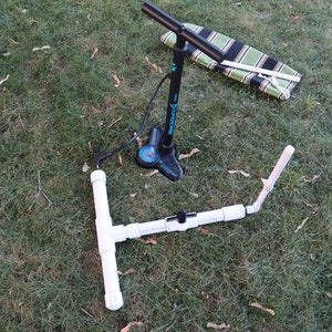 May include: A black foot pump with a blue and black handle, a white PVC pipe frame, and a striped blanket on the grass.